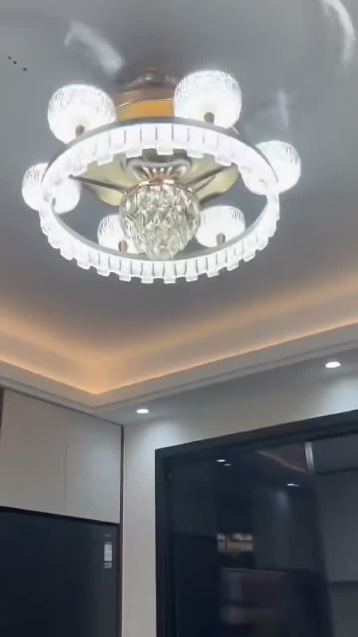 A round ceiling fan light with textured shades, hanging accents, and gold-toned details, shown from below.