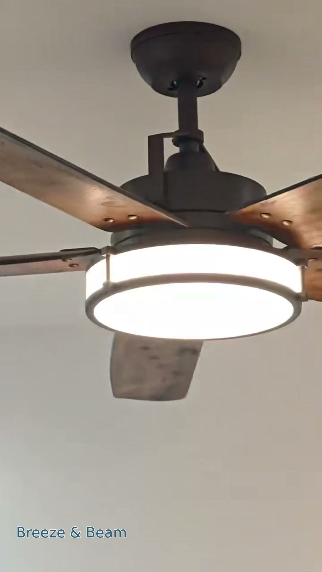 Close-up of a ceiling fan with brown blades with a wood-grain look, a dark housing, and an illuminated drum-style light.